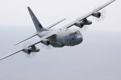 Photo of the WC-130J plane in flight. It is a 4 engine propeller plane painted grey.