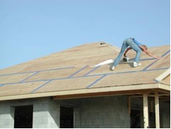 Photo of a worker installing tape over the seams in a roof’s plywood to minimize water intrusion.
